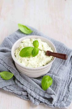 a white bowl filled with cream and green leaves on top of a blue towel next to a wooden spoon