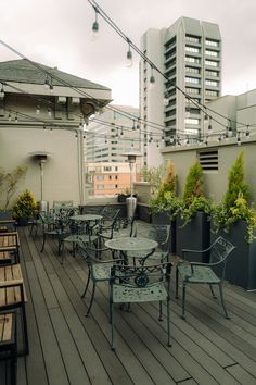 an outdoor patio with tables and chairs on top of the wooden floored area, surrounded by high rise buildings