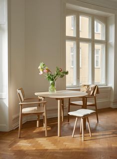 a table and chairs in front of a window with flowers on the table next to it