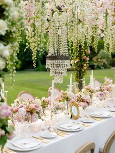 a table is set with white and pink flowers, candles, plates and napkins