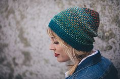 a woman wearing a knitted hat standing in front of a stone wall and looking off into the distance