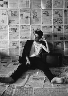 a man sitting on the floor in front of a wall covered with newspapers and newspaper clippings