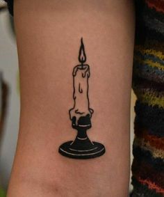 a small candle tattoo on the ankle is shown in black and grey ink, with a single burning candle at the top