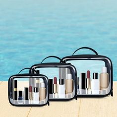 three cosmetic bags sitting on top of a wooden table next to a swimming pool with water in the background