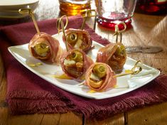 several wrapped figs and olive bites on a white plate