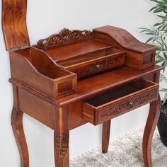 a wooden desk with a mirror on the top and an ornate drawer underneath it, in front of a potted plant