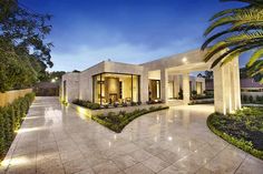 the entrance to a home at night with palm trees and landscaping in front of it