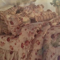 a bed covered in lots of pillows and blankets next to a wall with flowers on it