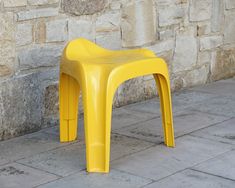 a yellow plastic chair sitting on top of a stone floor next to a brick wall