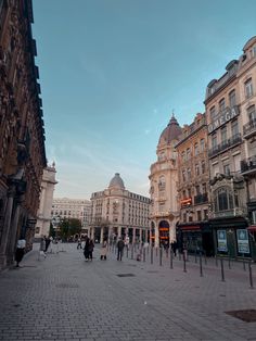 people are walking down the street in an old european city with tall buildings on either side