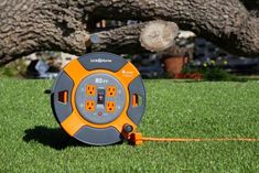 an orange and gray corded device on the grass in front of a large tree