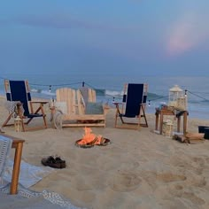 a fire pit sitting on top of a sandy beach next to the ocean with chairs