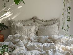 an unmade bed with white linens and green plants on the wall behind it