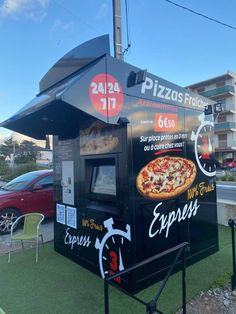 an outdoor pizza kiosk on the side of a road with cars in the background