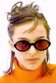 a young woman wearing sunglasses and an orange turtle neck sweater is looking at the camera