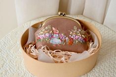 a small purse with an embroidered rabbit on it sitting in a round box next to a curtain