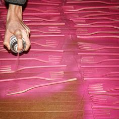 a person holding a can on top of a pink sheet of paper that has been cut into smaller strips