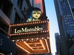 the marquee for les miserables is lit up in front of tall buildings