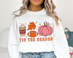 a woman wearing a white sweatshirt with the words tis the season on it and pumpkins