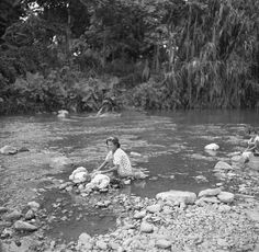 an old black and white photo of a woman sitting on rocks in the river with her dog