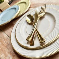 two plates with gold rimmed forks and spoons on top of each other, sitting on a wooden table