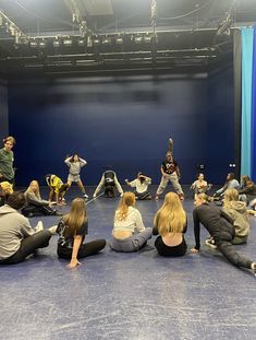 a group of people sitting on the floor in front of a blue wall doing yoga