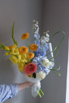 a person holding a bouquet of flowers in front of a white wall with grey walls