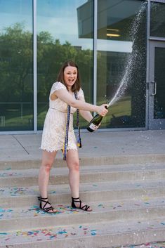 a woman holding a bottle of champagne and spraying it with her hands on the steps