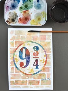 an artist's palette and watercolors are sitting on a table next to a piece of paper with the number nine painted in it