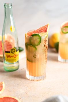 two glasses filled with drinks sitting on top of a table next to sliced grapefruits