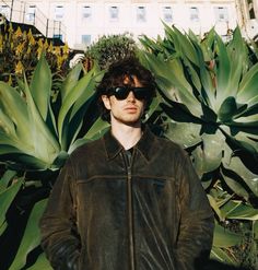 a man wearing sunglasses standing in front of plants