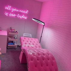 a pink room with a bed, desk and chair next to a neon sign that says all you need is too lager