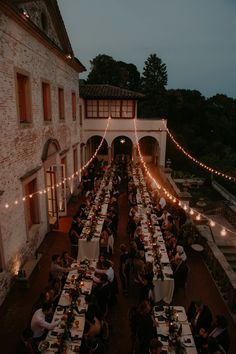 an outdoor dining area with long tables and string lights strung across the building's roof