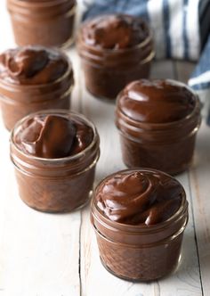 four jars filled with chocolate frosting sitting on top of a wooden table