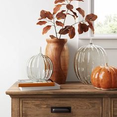 two glass pumpkins sitting on top of a wooden table next to a window and books