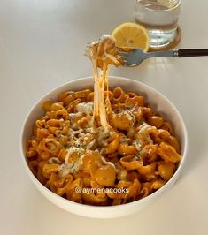 a white bowl filled with pasta covered in cheese and sauce next to a lemon wedge