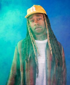 a man with dreadlocks and a yellow hat is posing in front of a blue background