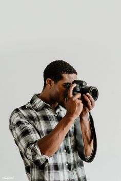 a man holding a camera up to his face and looking into the distance while wearing a plaid shirt