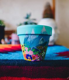 a blue flower pot sitting on top of a colorful table cloth next to a plant