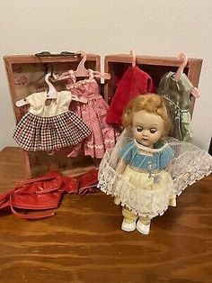 an old doll and some other dolls on a wooden table in front of a suitcase