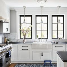 a kitchen with white cabinets, black counter tops and blue rug on the floor in front of two windows