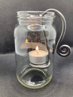 a glass jar with a candle inside on a gray surface and the lid is open