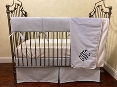 a baby crib with two white sheets on top of it and one has a monogrammed blanket