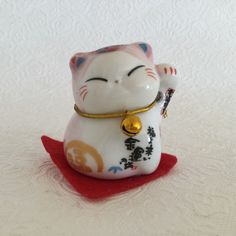 a small white cat figurine sitting on top of a red carpeted floor