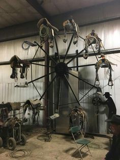 a large metal clock sitting inside of a building next to a wall filled with horse saddles