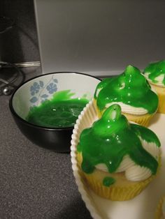 cupcakes with green icing sitting on top of a white plate next to a black bowl