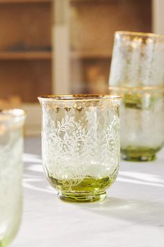 three glass cups sitting on top of a white table covered in green liquid and gold rims