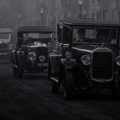 an old time car driving down the road in front of other cars on a foggy day