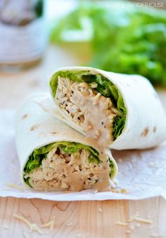 two wraps filled with chicken and lettuce sitting on top of a wooden table