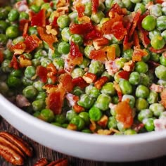 a bowl filled with peas and bacon on top of a wooden table next to pecans